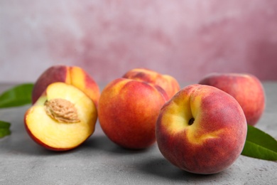 Photo of Fresh peaches and leaves on grey table against pink background