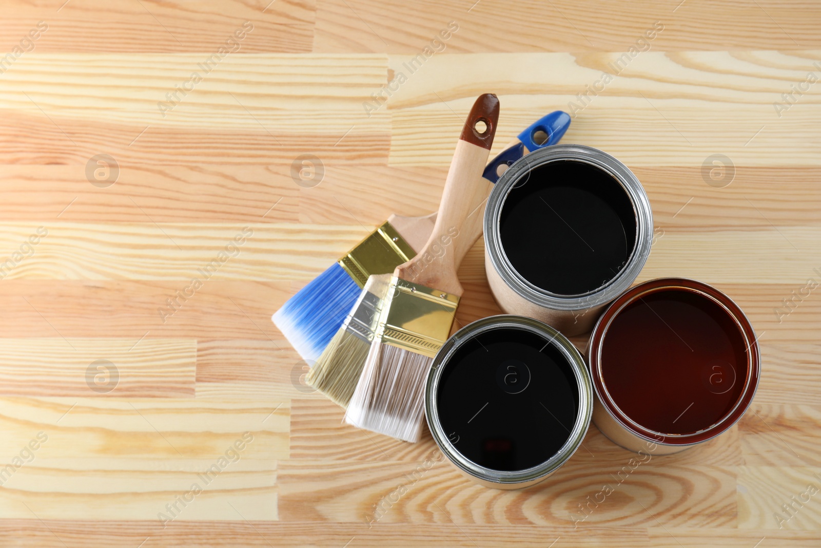 Photo of Can with different wood stains and brushes on wooden surface, flat lay. Space for text