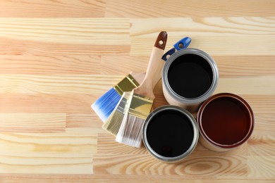 Can with different wood stains and brushes on wooden surface, flat lay. Space for text