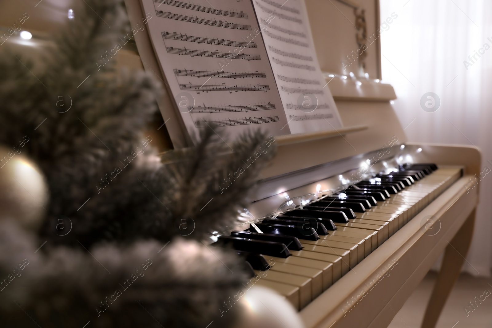 Photo of White piano with festive decor and note sheets indoors, closeup. Christmas music