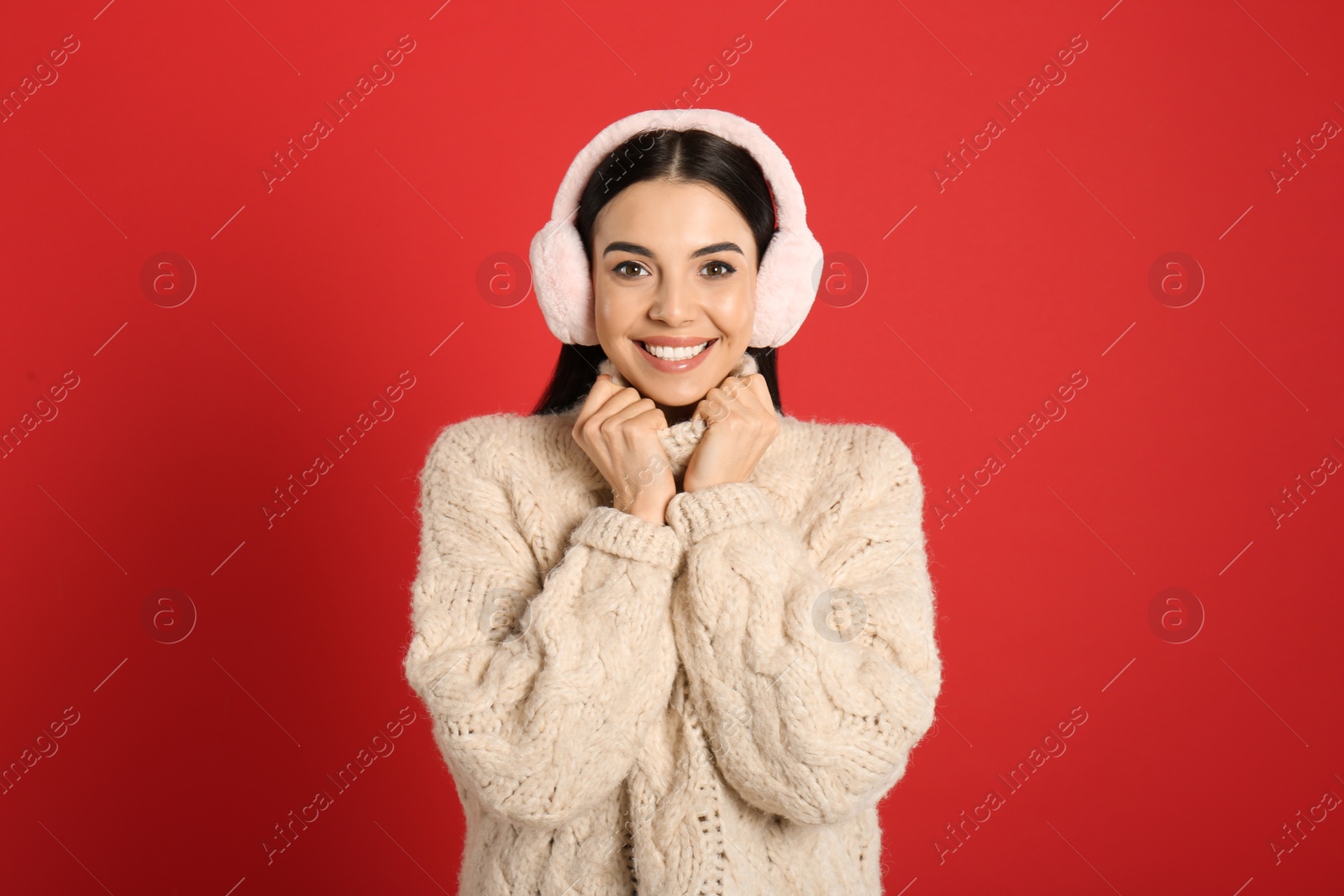 Photo of Beautiful young woman wearing earmuffs on red background