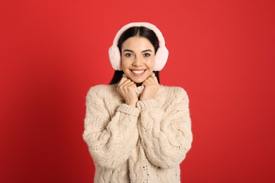 Beautiful young woman wearing earmuffs on red background