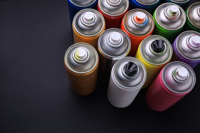 Cans of different graffiti spray paints on black background, above view