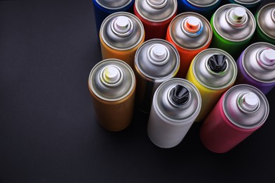 Photo of Cans of different graffiti spray paints on black background, above view