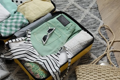 Photo of Open suitcase with summer clothes and accessories on floor