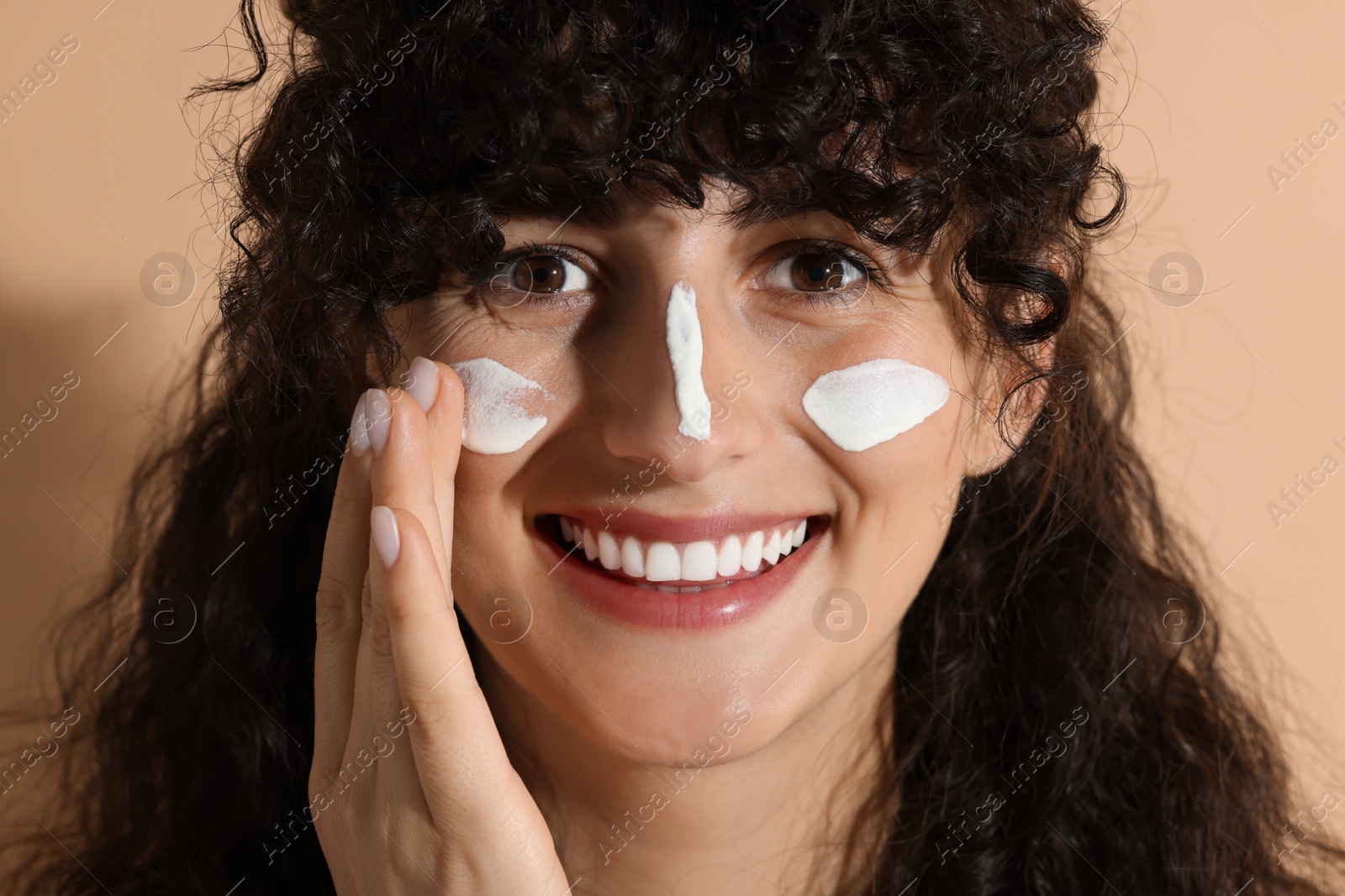 Photo of Beautiful young woman applying sun protection cream onto face on beige background