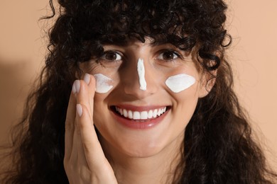 Beautiful young woman applying sun protection cream onto face on beige background