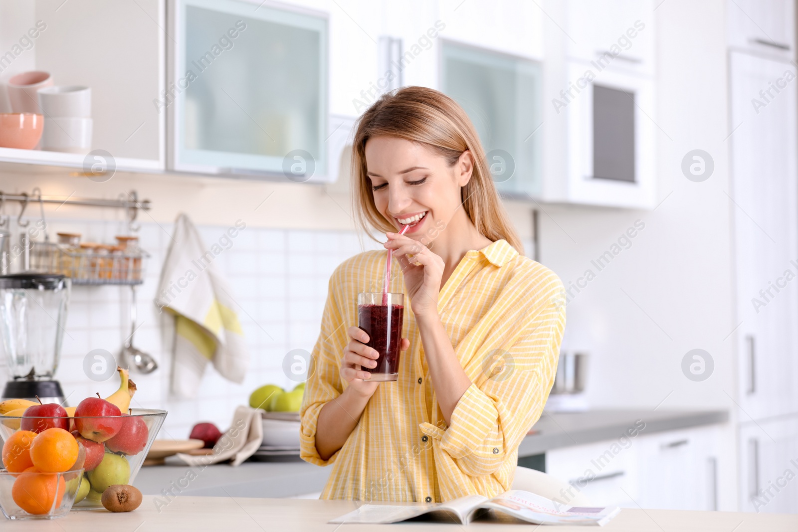 Photo of Young woman with glass of tasty healthy smoothie at table in kitchen