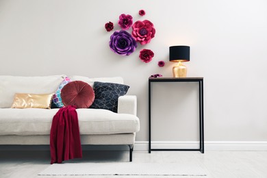 Comfortable sofa and table near wall with floral decor in living room