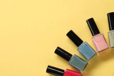 Colorful nail polishes in bottles on yellow background, flat lay. Space for text