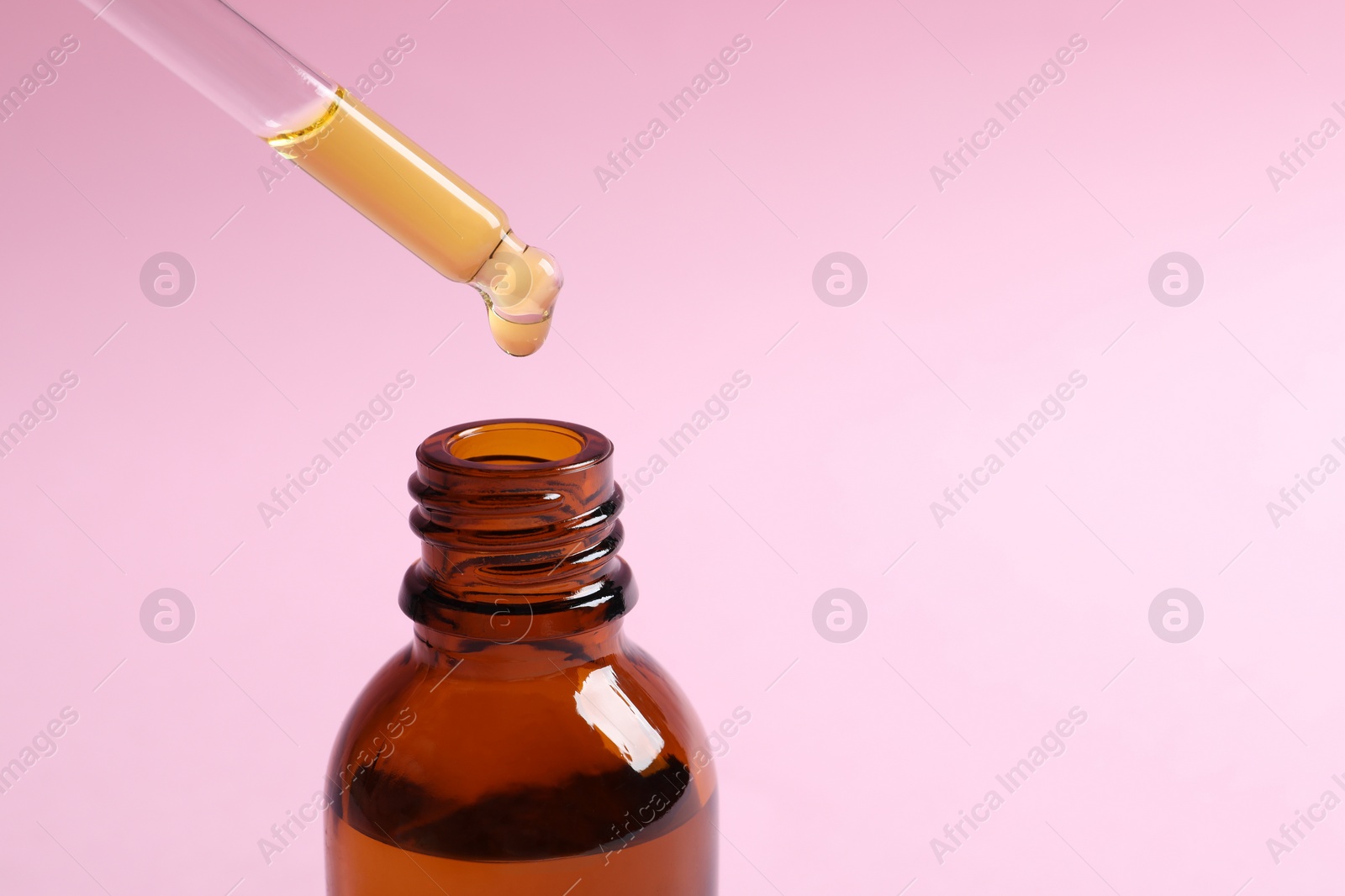 Photo of Dripping cosmetic oil from pipette into bottle on pink background, closeup. Space for text