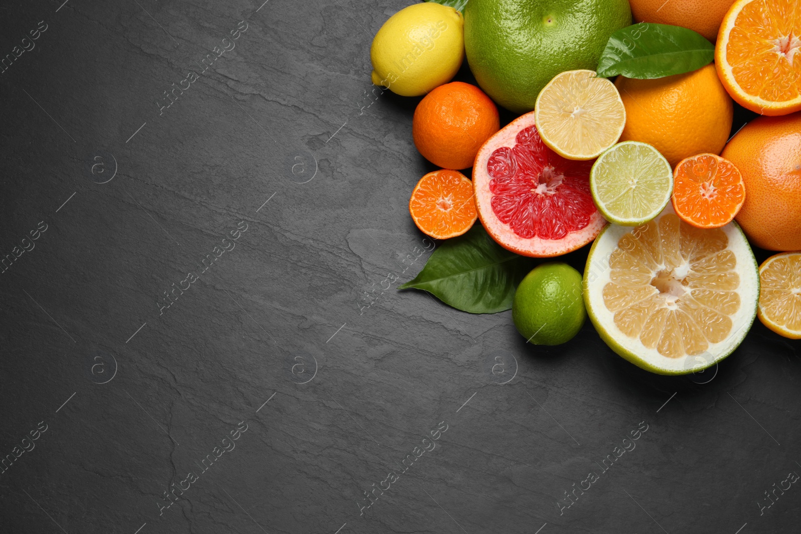 Photo of Different ripe citrus fruits with green leaves on black table, flat lay. Space for text