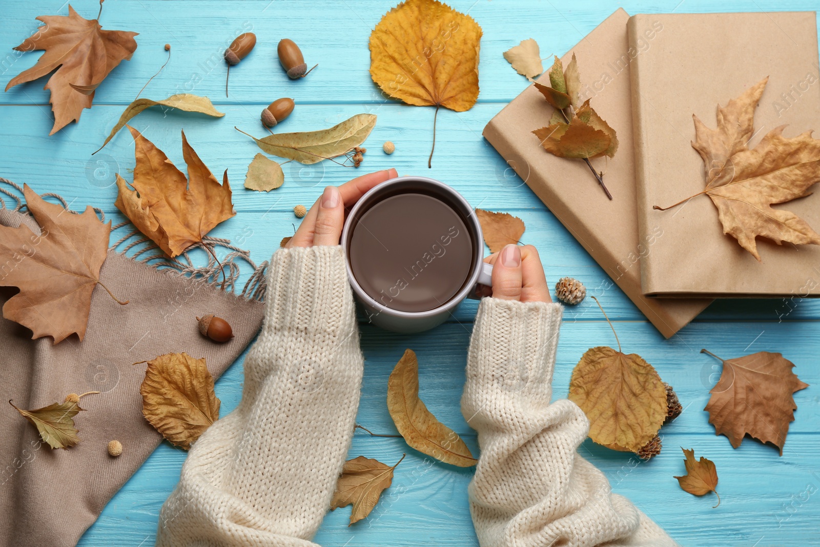 Photo of Woman with cup of hot drink at light blue wooden table, top view. Cozy autumn atmosphere