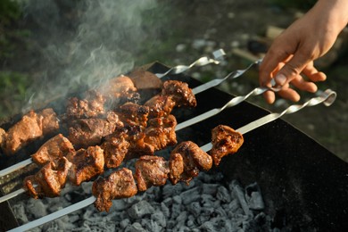 Photo of Man cooking delicious meat on brazier outdoors, closeup