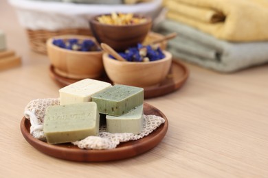 Tray with soap bars and bowls of dry flowers on light wooden table, space for text. Spa therapy