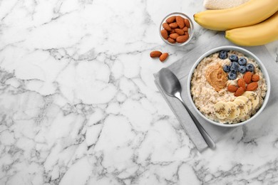 Photo of Tasty oatmeal porridge with toppings served on white marble table, flat lay. Space for text