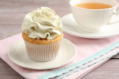 Photo of Tasty cupcake with vanilla cream on pink wooden table, closeup