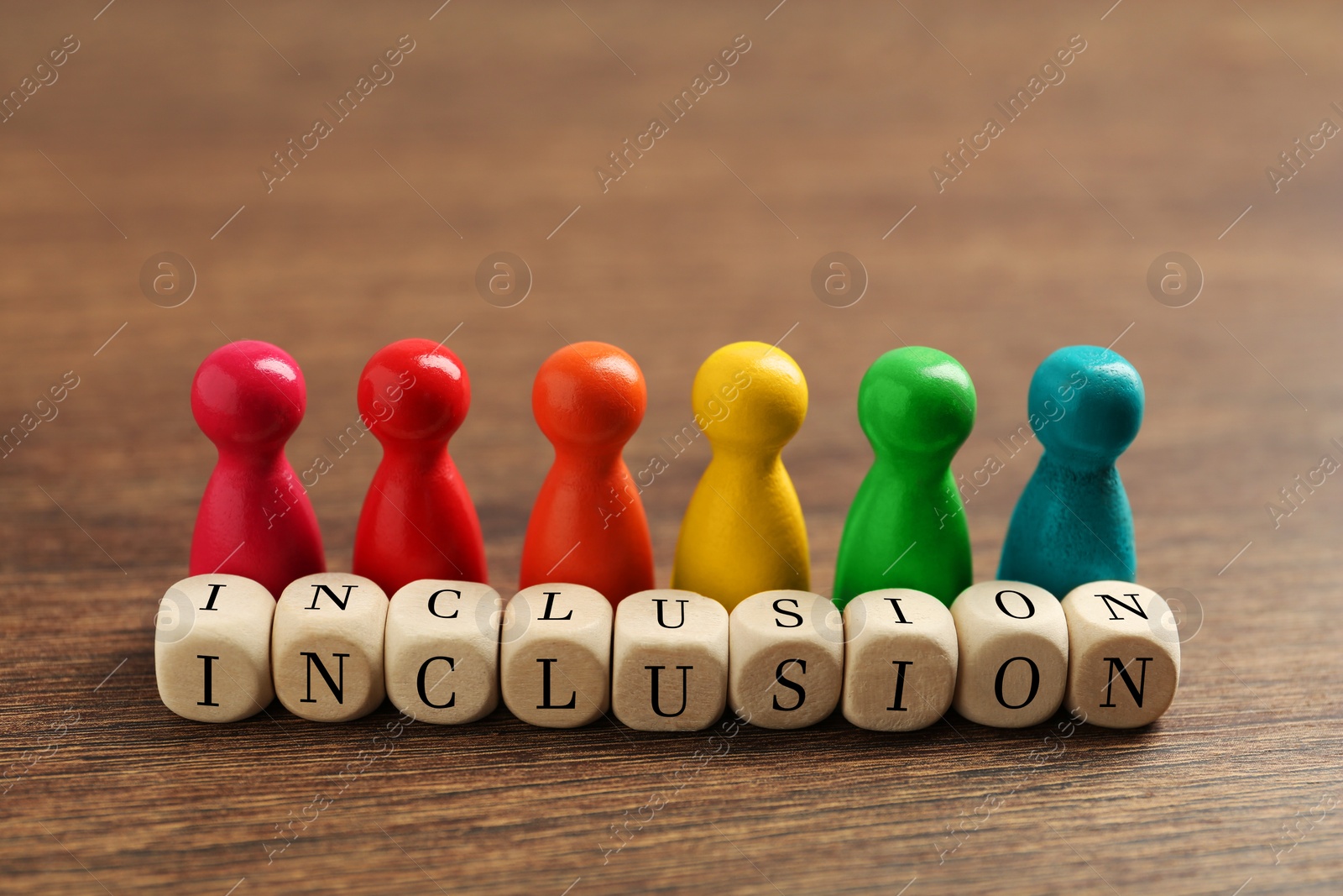 Photo of Colorful pawns and cubes with word Inclusion on wooden table, closeup