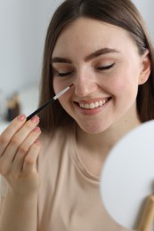 Photo of Smiling woman drawing freckles with brush indoors