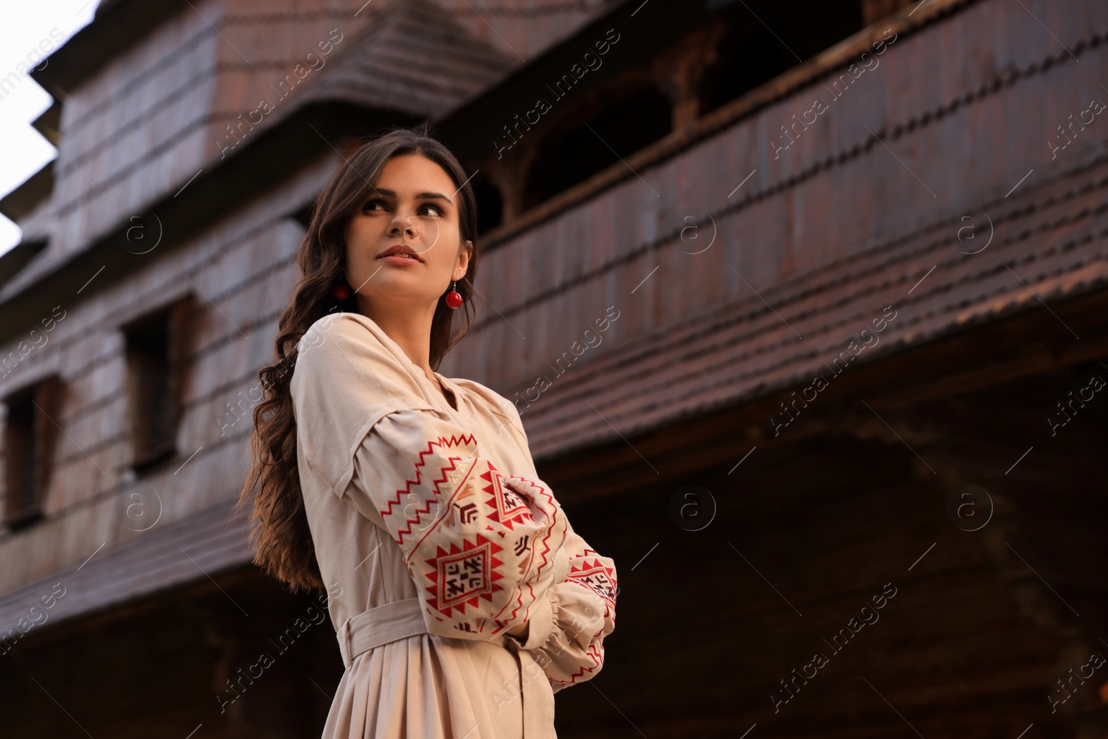 Photo of Beautiful woman wearing embroidered dress near old wooden church in village. Ukrainian national clothes