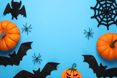 Flat lay composition with bats, pumpkins and spiders on light blue background, space for text. Halloween celebration