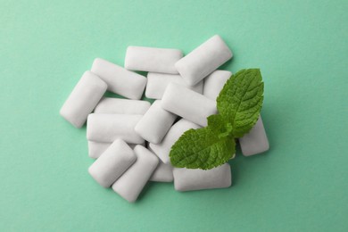 Photo of Tasty white chewing gums and mint leaves on turquoise background, top view