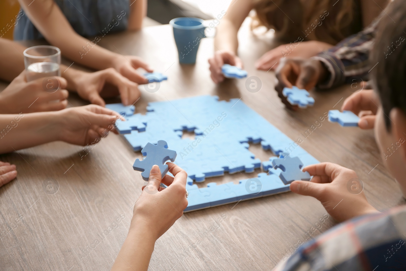 Photo of People with puzzle at table, closeup of hands. Unity concept