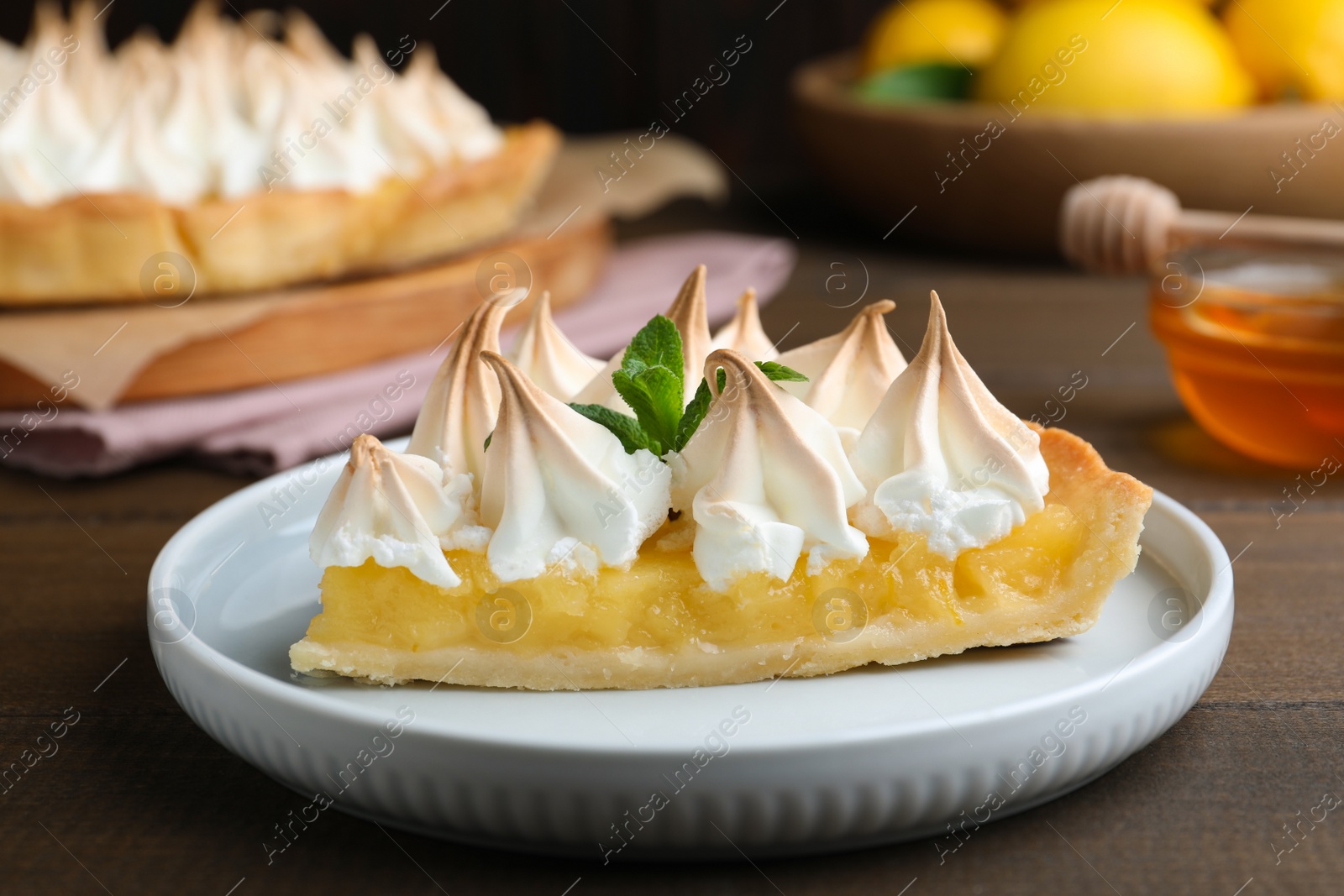 Photo of Piece of delicious lemon meringue pie with mint served on wooden table, closeup