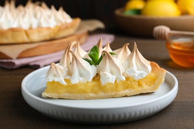 Photo of Piece of delicious lemon meringue pie with mint served on wooden table, closeup