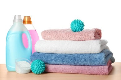 Photo of Dryer balls, detergents and stacked clean towels on wooden table against white background