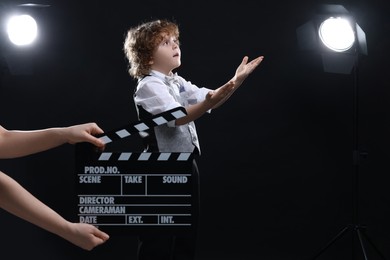 Photo of Cute boy performing while second assistant camera holding clapperboard on stage. Little actor