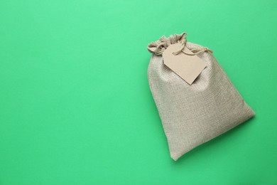 Photo of Tied burlap bag with tag on green background, top view. Space for text