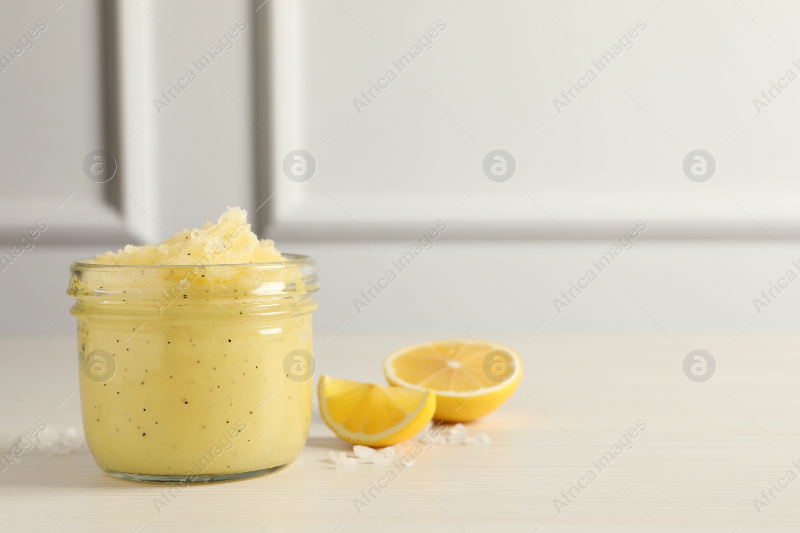 Photo of Body scrub in glass jar and lemon on light wooden table, space for text