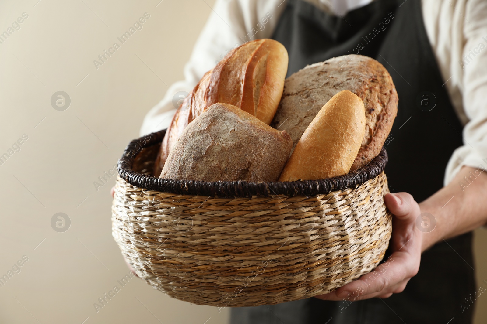 Photo of Man holding wicker basket with different types of bread on beige background, closeup