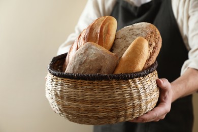 Photo of Man holding wicker basket with different types of bread on beige background, closeup