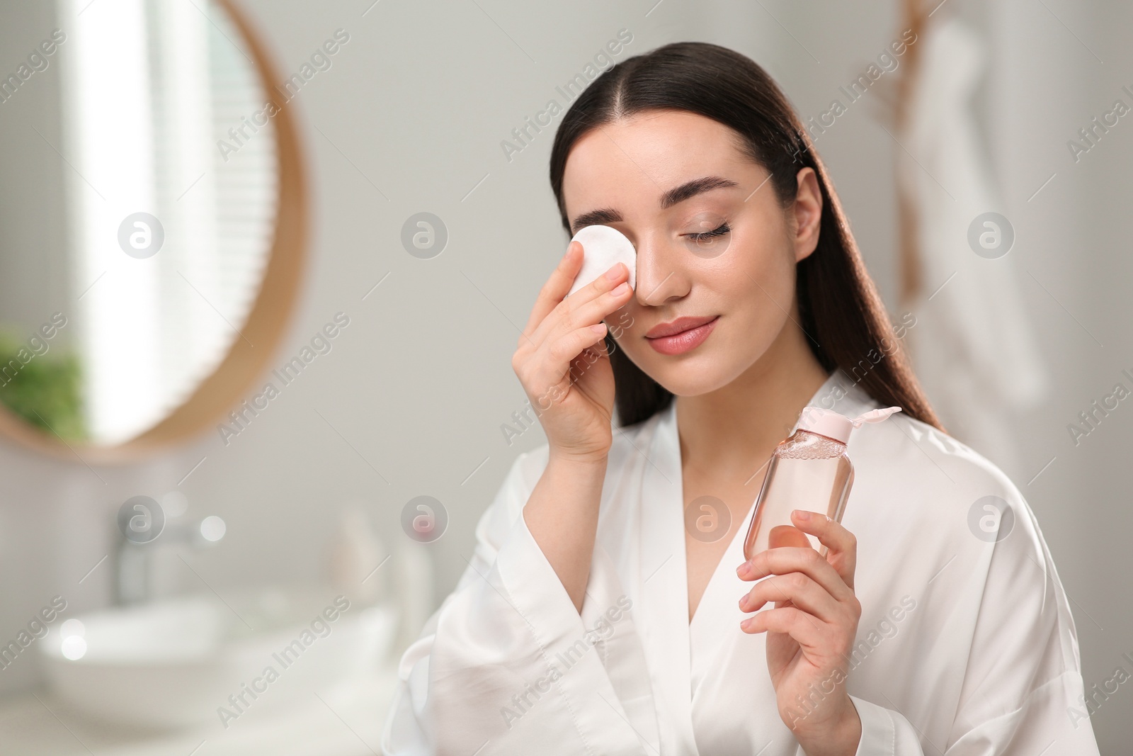 Photo of Beautiful woman removing makeup with cotton pad indoors