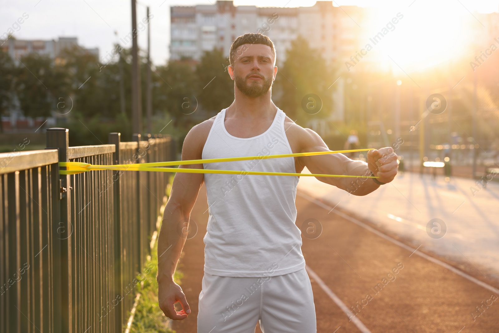 Photo of Muscular man doing exercise with elastic resistance band outdoors at sunset