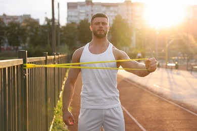 Muscular man doing exercise with elastic resistance band outdoors at sunset