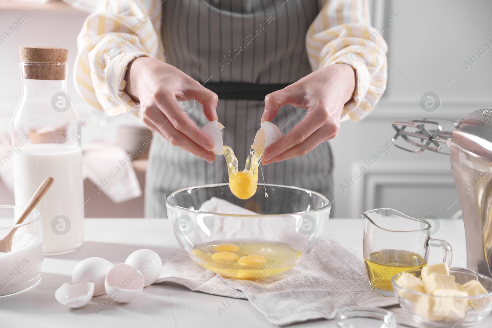 Photo of Making dough. Woman breaking egg at white table in kitchen, closeup