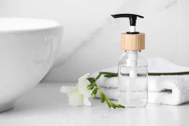 Photo of Bottle with dispenser cap, towel and beautiful flower on white table in bathroom, closeup