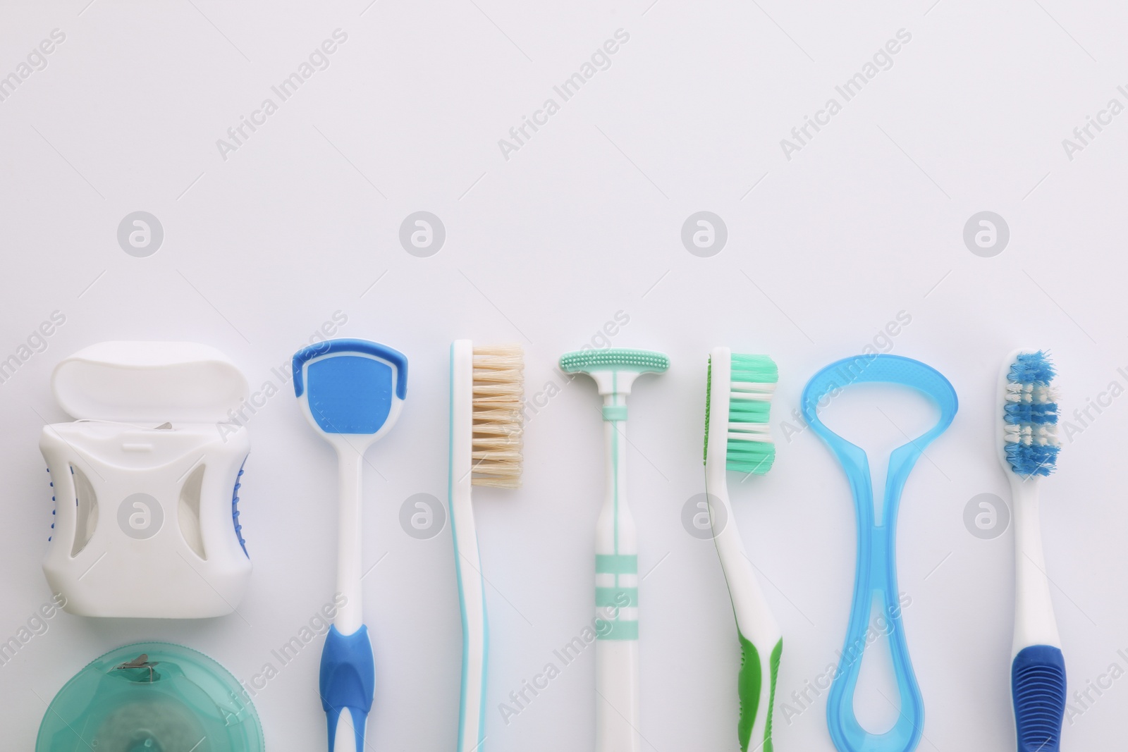 Photo of Different tongue cleaners, dental flosses and toothbrushes on white background, top view