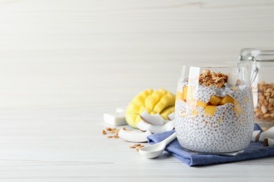 Photo of Delicious chia pudding with granola and mango on white wooden table, space for text