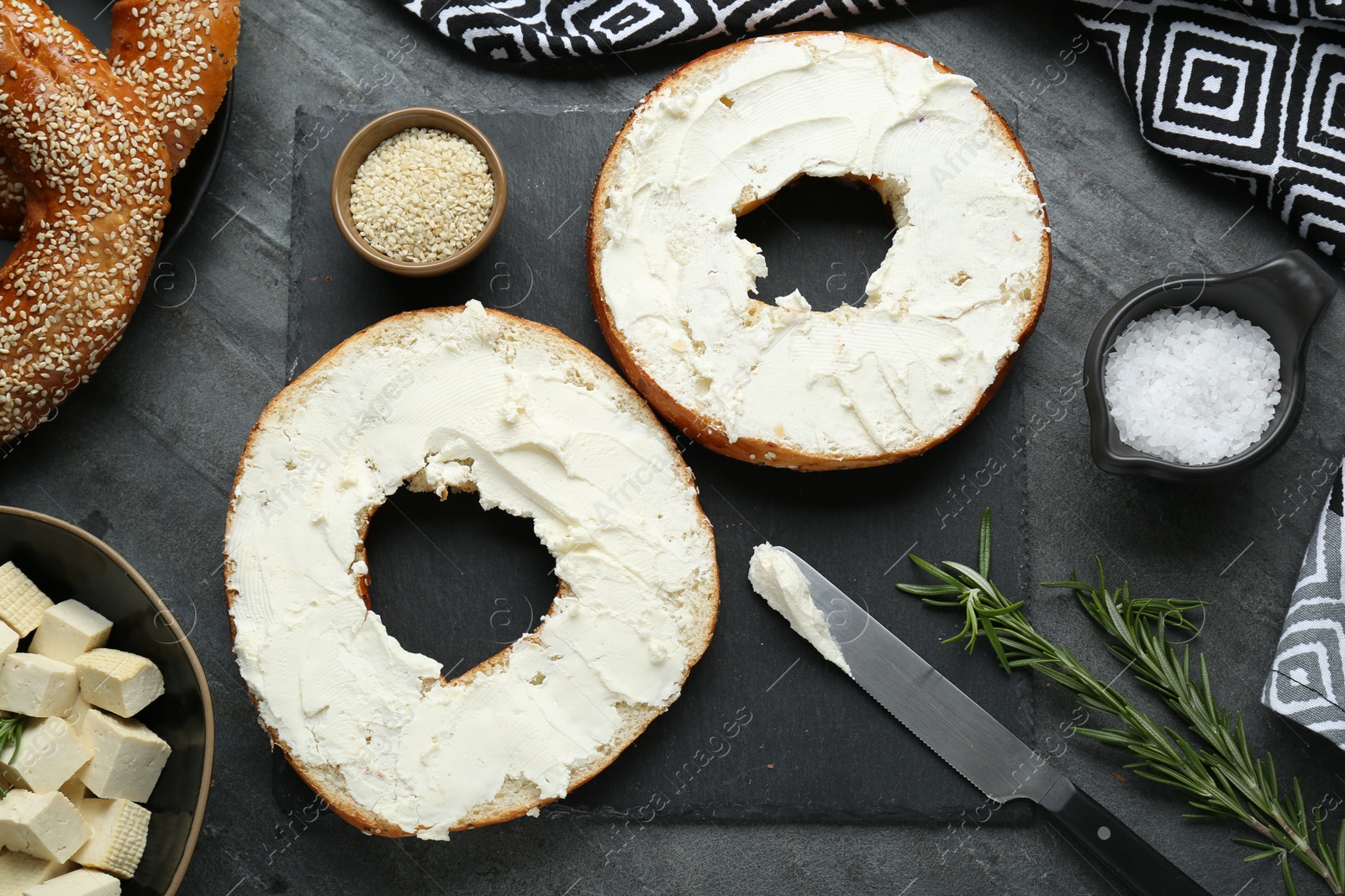 Photo of Delicious bagels with tofu cream cheese, sesame seeds and salt on black table, flat lay