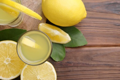 Tasty limoncello liqueur, lemons and green leaves on wooden table, top view. Space for text