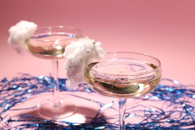 Photo of Tasty cocktails in glasses decorated with cotton candy and blue shiny streamers on pink background, closeup