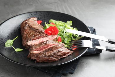 Photo of Delicious grilled beef meat served with greens on grey table, closeup