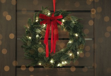 Photo of Beautiful Christmas wreath with red bow and festive lights hanging on door indoors. Bokeh effect