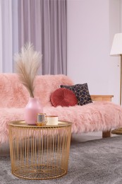 Vase and candles on coffee table near sofa in stylish room. Interior design