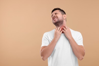 Photo of Allergy symptom. Man scratching his neck on light brown background. Space for text