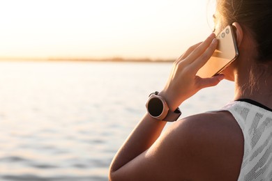 Photo of Woman with fitness tracker talking on phone near river, closeup. Space for text